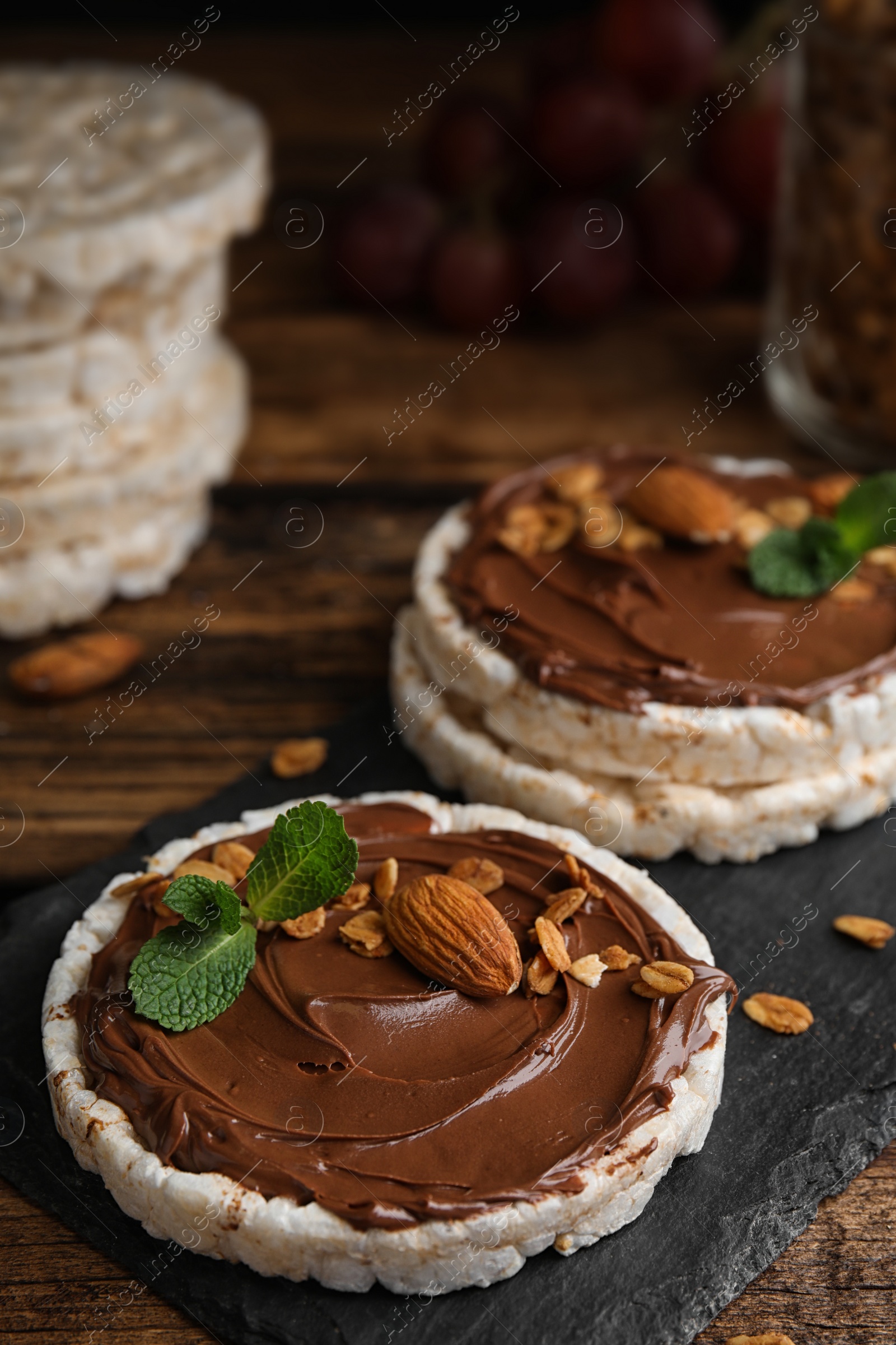 Photo of Puffed rice cakes with chocolate spread, nuts and mint on wooden table