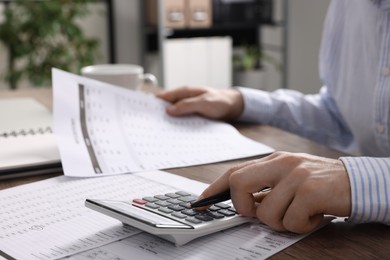Man working with data using calculator at wooden table indoors, closeup