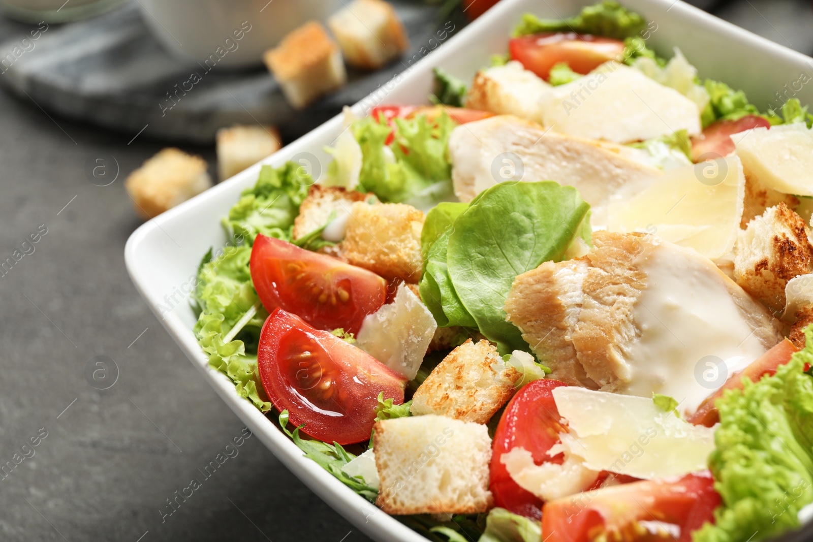 Photo of Delicious fresh Caesar salad in bowl on grey table, closeup