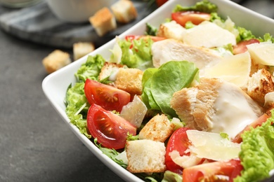 Photo of Delicious fresh Caesar salad in bowl on grey table, closeup