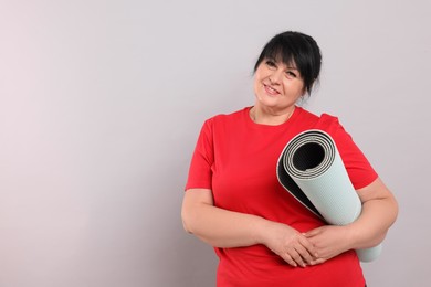 Photo of Happy overweight mature woman with yoga mat on grey background, space for text