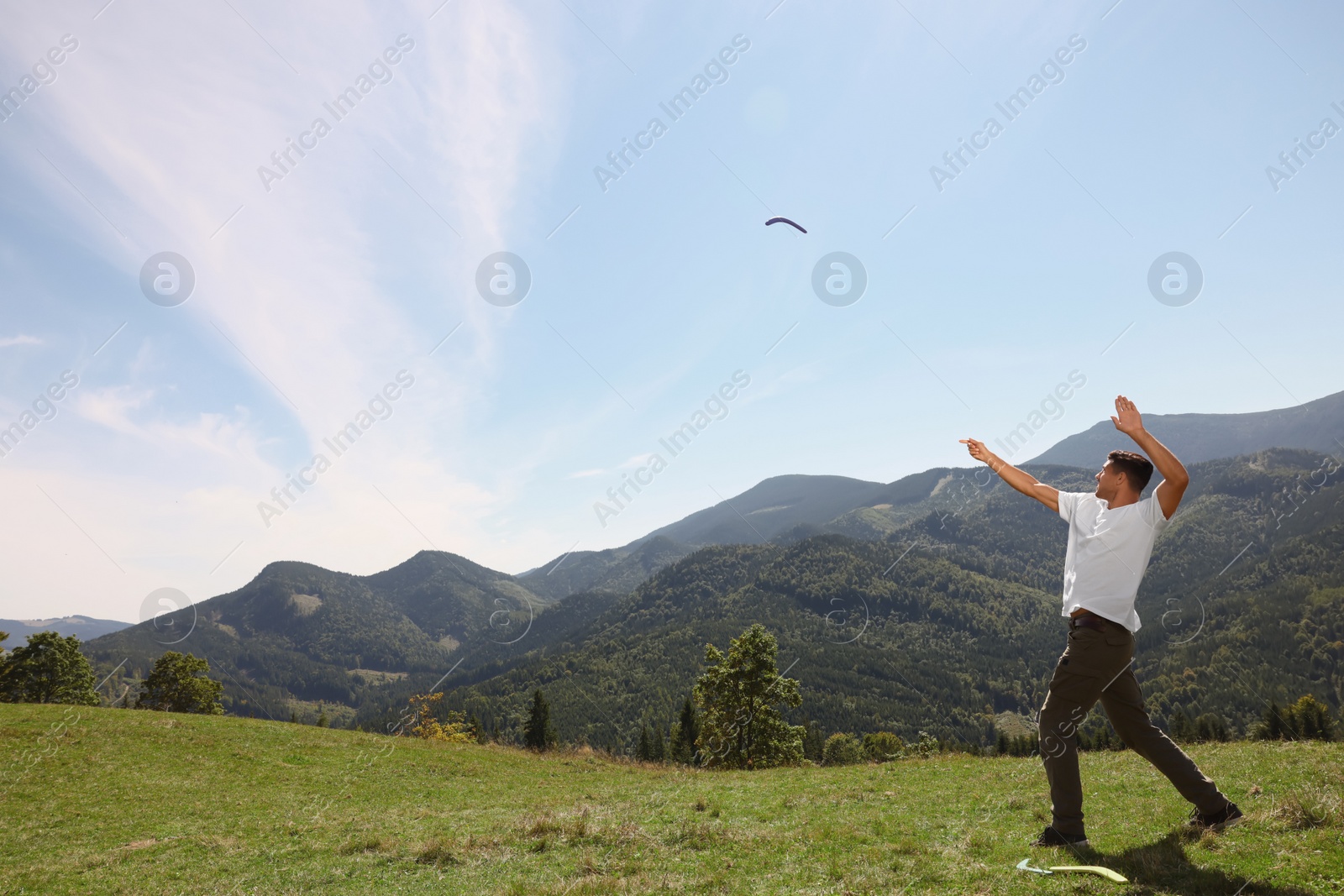 Photo of Man throwing boomerang in mountains on sunny day. Space for text