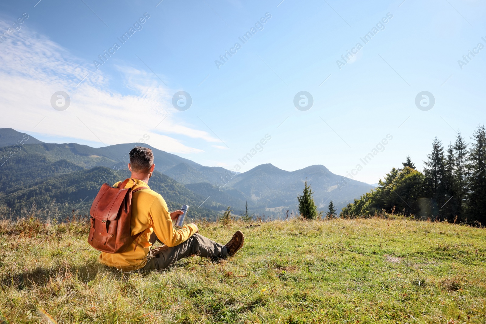 Photo of Tourist with thermos and backpack enjoying beautiful mountain landscape, back view.