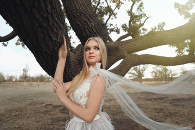 Beautiful girl wearing fairy dress near tall tree outdoors