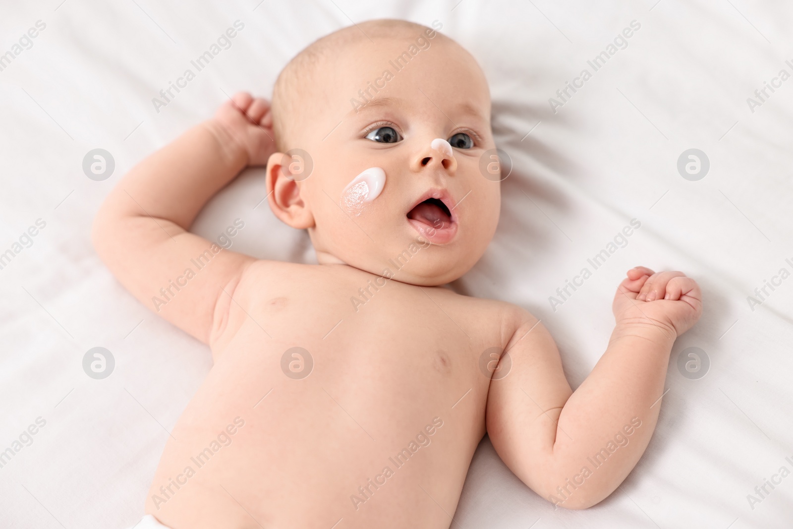 Photo of Cute little baby with cream on face on white blanket, above view