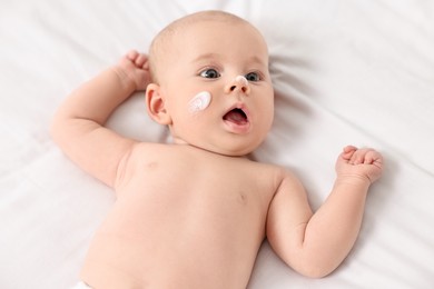 Cute little baby with cream on face on white blanket, above view