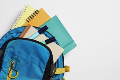 Backpack with different school stationery on white background, top view. Space for text