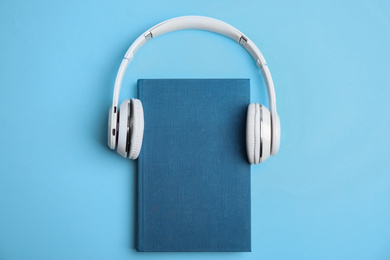 Book and modern headphones on light blue background, top view