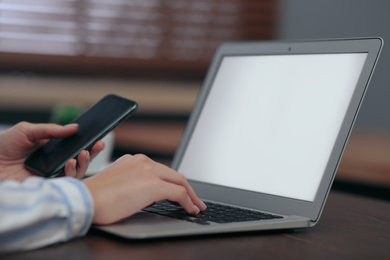 Woman with mobile phone working on modern laptop at table, closeup