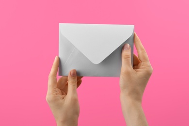 Photo of Woman holding white paper envelope on pink background, closeup