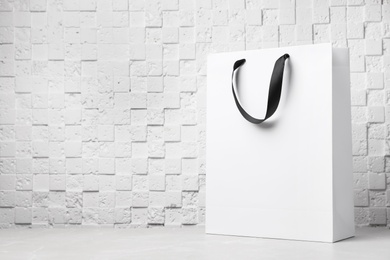 Paper shopping bag with ribbon handles on table near white wall. Mockup for design