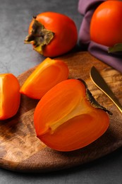 Photo of Delicious ripe persimmons and knife on wooden board, closeup