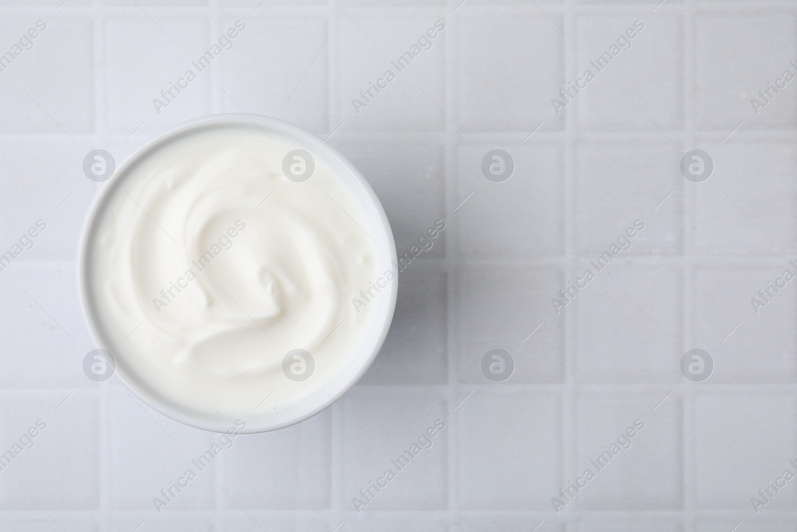 Photo of Delicious natural yogurt in bowl on white tiled table, top view. Space for text