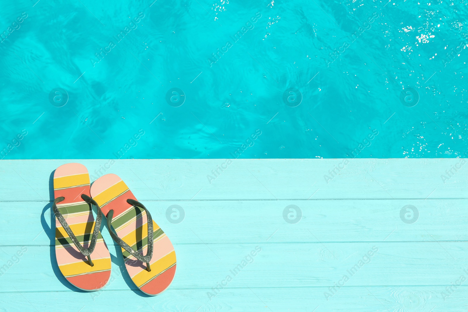 Photo of Slippers on wooden deck near swimming pool, top view with space for text. Beach accessory