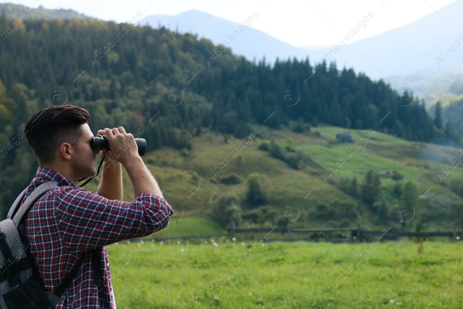 Photo of Man with backpack looking through binoculars in mountains