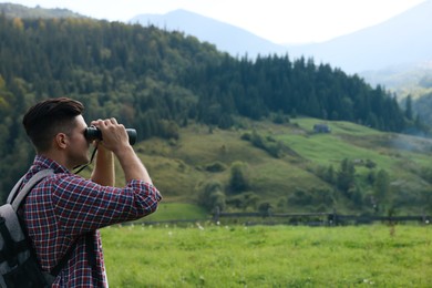 Man with backpack looking through binoculars in mountains