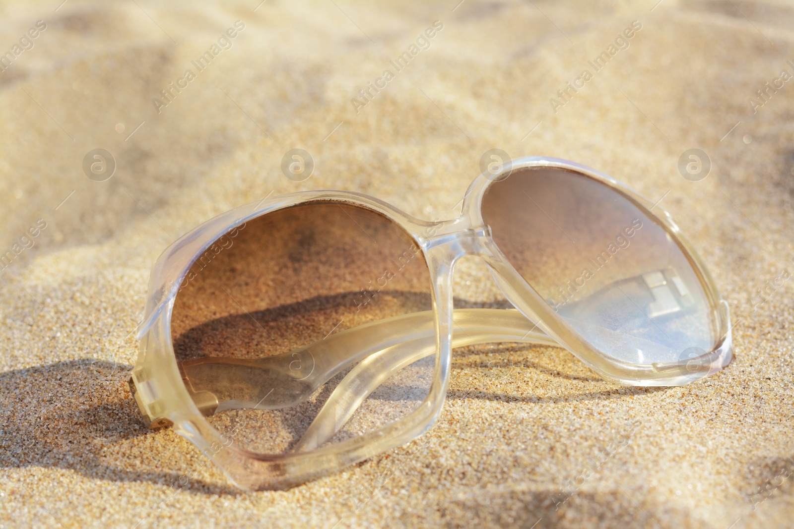 Photo of Stylish sunglasses on sandy beach, closeup view
