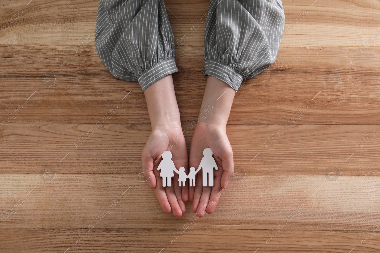 Photo of Woman holding figure of family at wooden table, top view