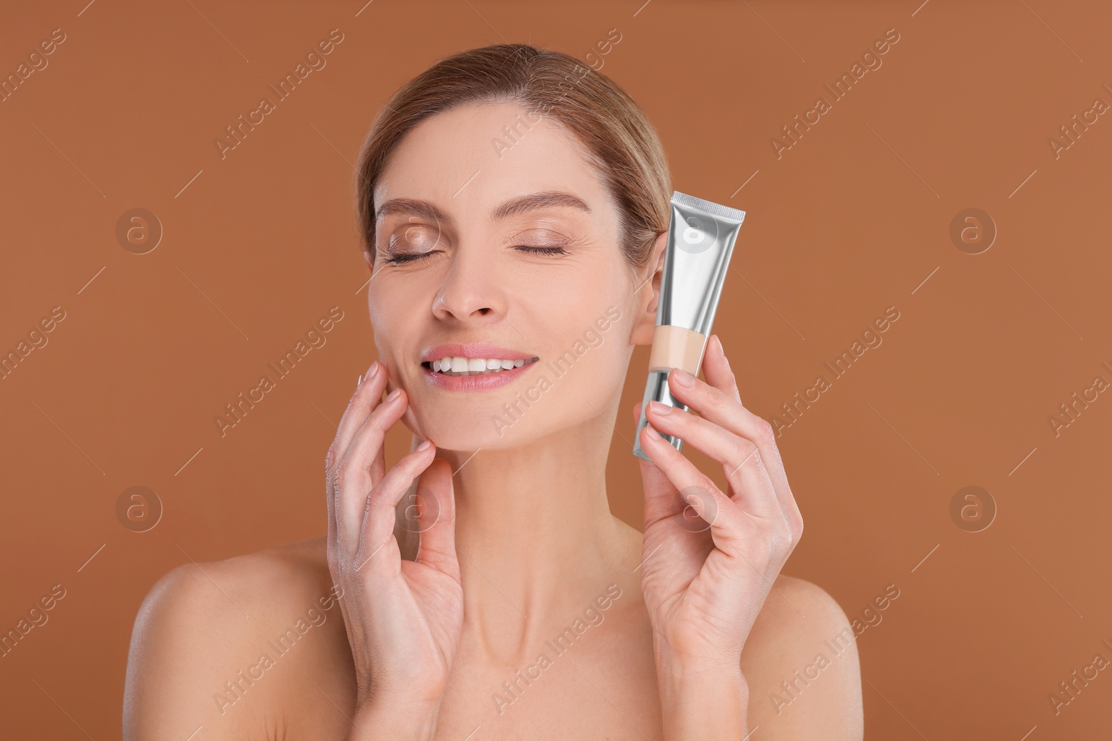 Photo of Woman holding tube of foundation on brown background