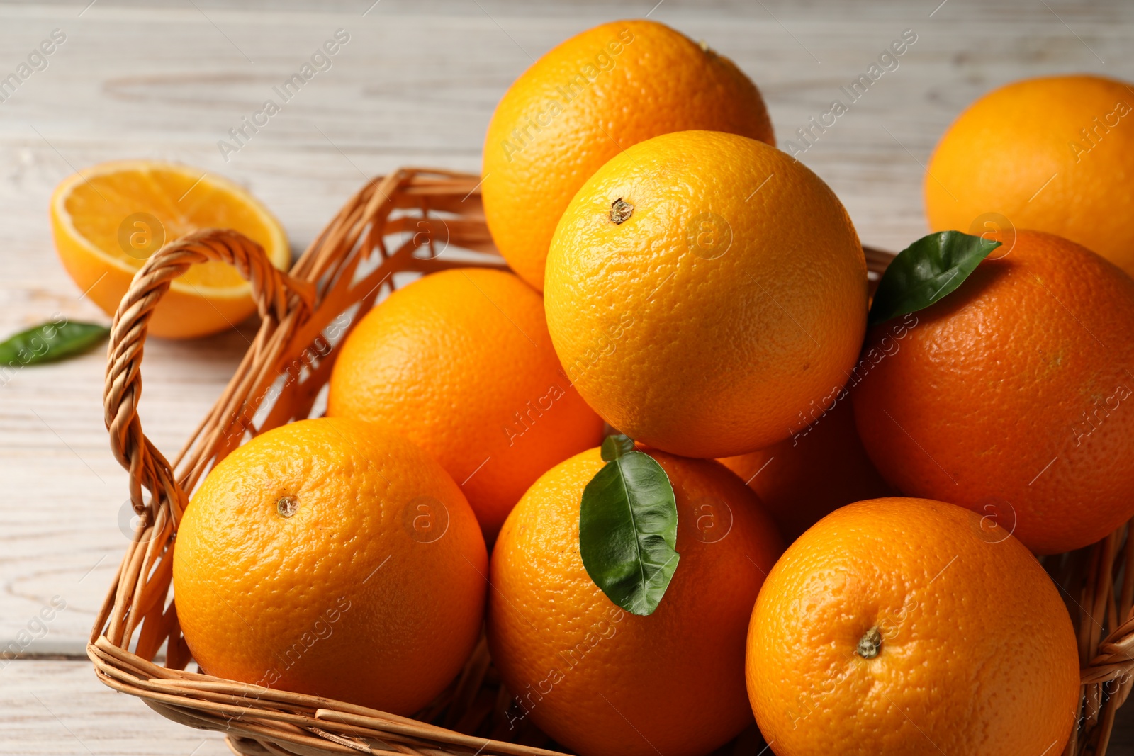 Photo of Many ripe oranges and green leaves on wooden table, closeup