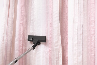 Photo of Removing dust from beautiful curtains with professional vacuum cleaner indoors