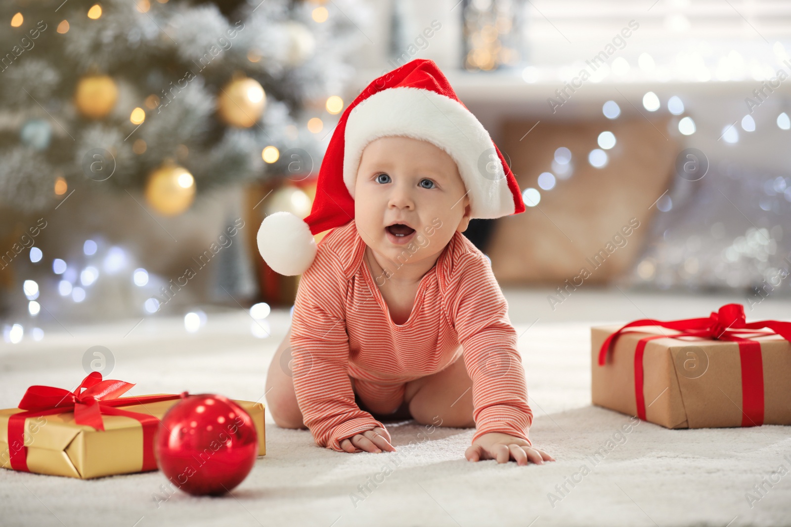 Photo of Little baby in Santa hat with Christmas decoration on floor at home