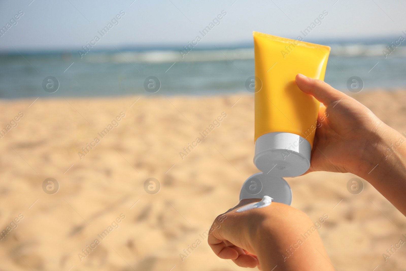 Photo of Child applying sunscreen near sea, closeup. Space for text. Sun protection care