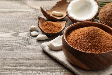 Natural coconut sugar in bowl on wooden table, space for text