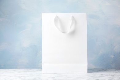 Photo of Paper shopping bag with ribbon handles on table against color background. Mockup for design