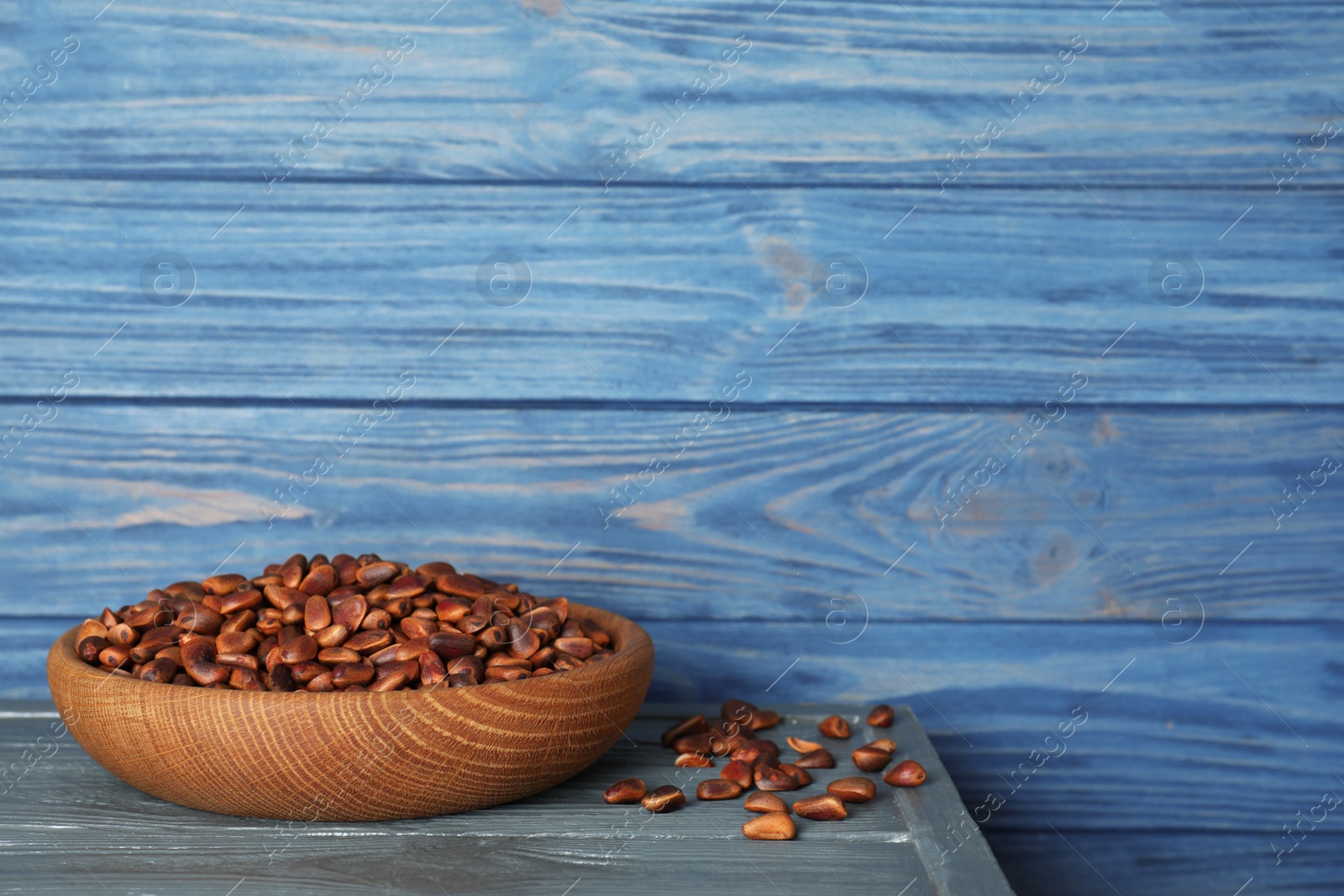 Photo of Dish with pine nuts on table against wooden background. Space for text