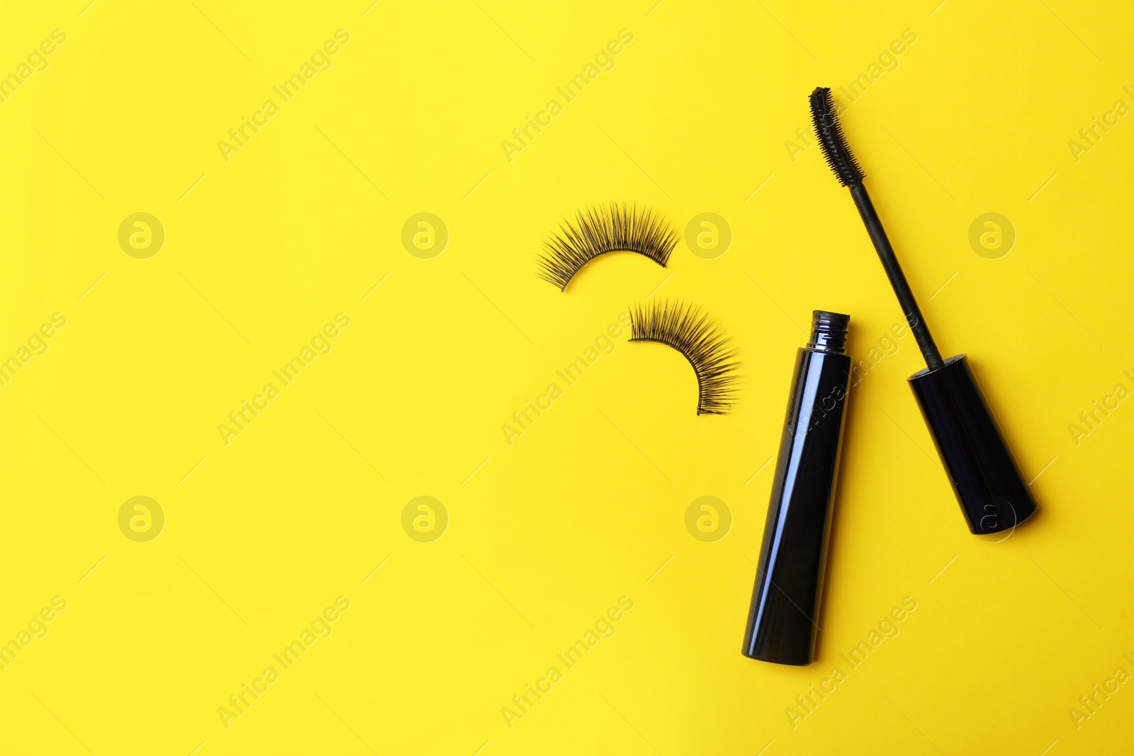 Photo of Black mascara and fake eyelashes on yellow background, flat lay with space for text. Makeup product