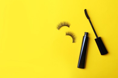 Black mascara and fake eyelashes on yellow background, flat lay with space for text. Makeup product