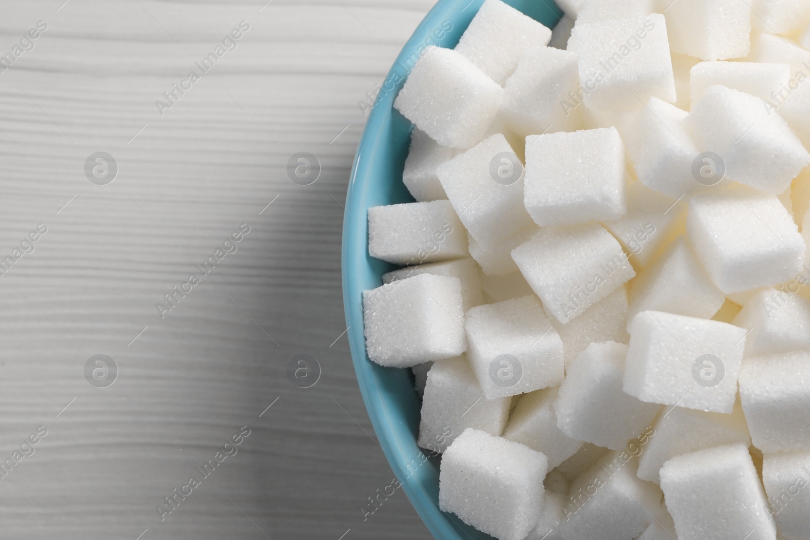 Photo of White sugar cubes in bowl on wooden table, top view. Space for text