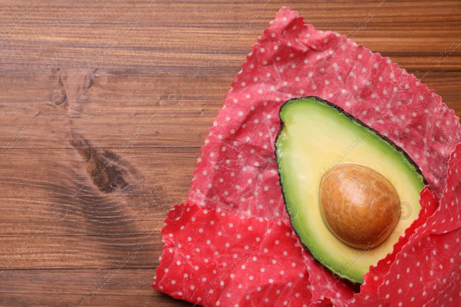 Photo of Half of avocado in beeswax food wrap on wooden table, top view. Space for text