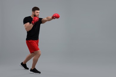 Photo of Man in boxing gloves fighting on grey background. Space for text