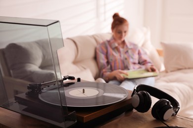 Photo of Young woman with vinyl discs in living room, focus on turntable