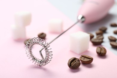 Pink milk frother wand, coffee beans and sugar cubes on color background, closeup