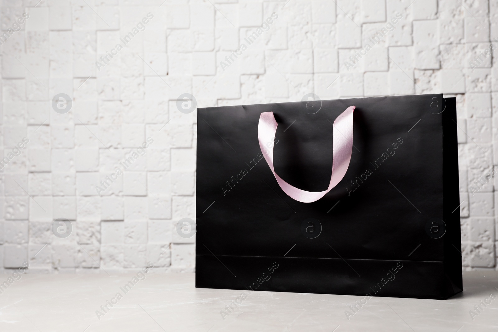 Photo of Paper shopping bag with ribbon handles on table near white wall. Mockup for design