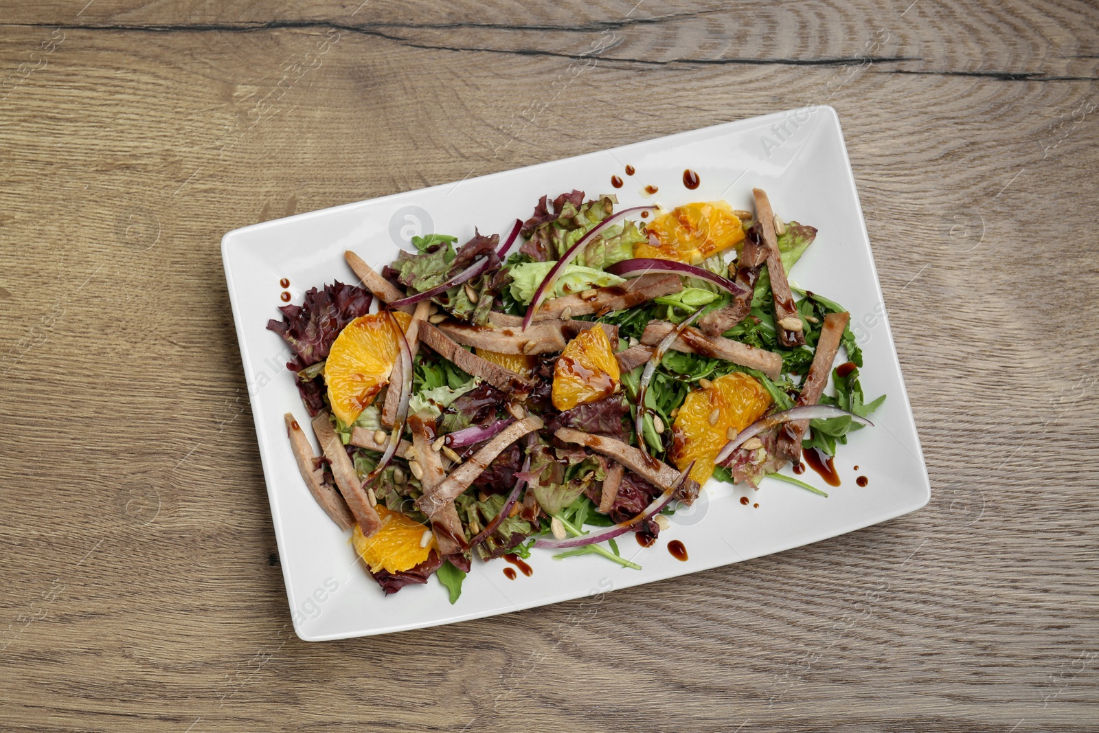 Photo of Delicious salad with beef tongue, orange and onion on wooden table, top view