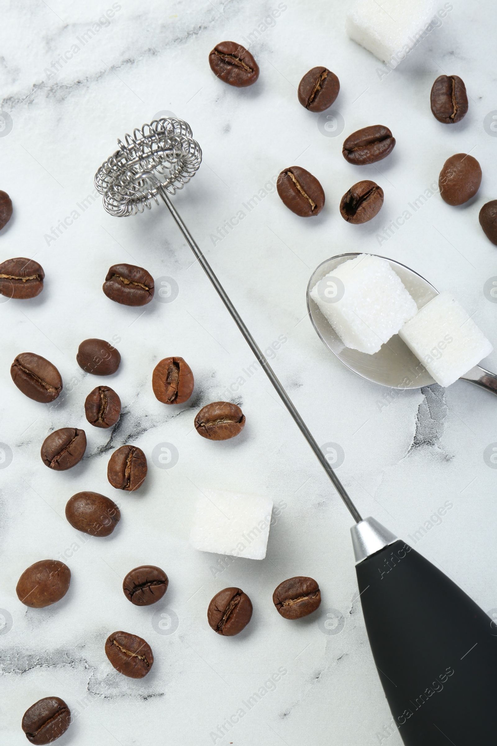 Photo of Black milk frother wand, sugar cubes and coffee beans on white marble table, flat lay