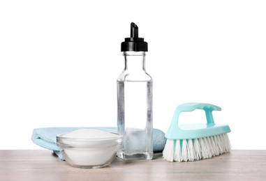 Photo of Natural cleaning products. Vinegar in bottle, baking soda, brush and rag on light wooden table against white background