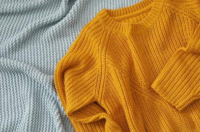 Cozy knitted sweater on blanket, above view. Space for text