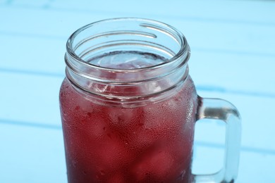 Mason jar of delicious iced hibiscus tea on light blue table, closeup