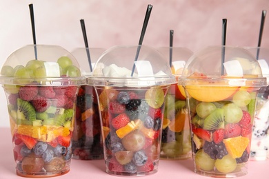 Photo of Fresh tasty fruit salad in plastic cups on pink table