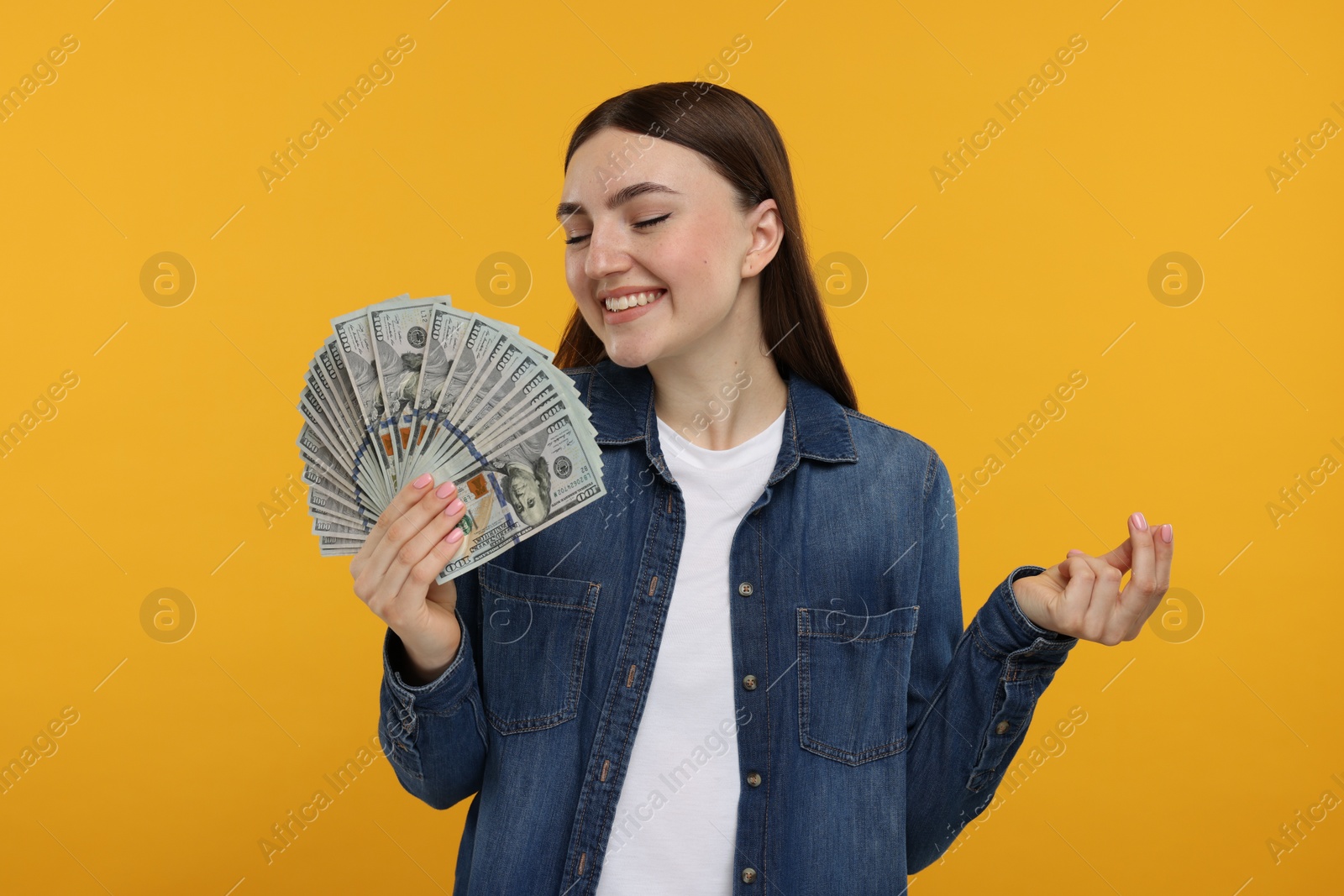 Photo of Happy woman with dollar banknotes on orange background