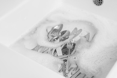 Photo of Washing silver spoons, forks and knives in kitchen sink with foam, above view