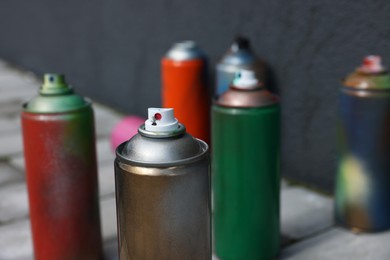 Cans of different spray paints near wall outdoors, closeup