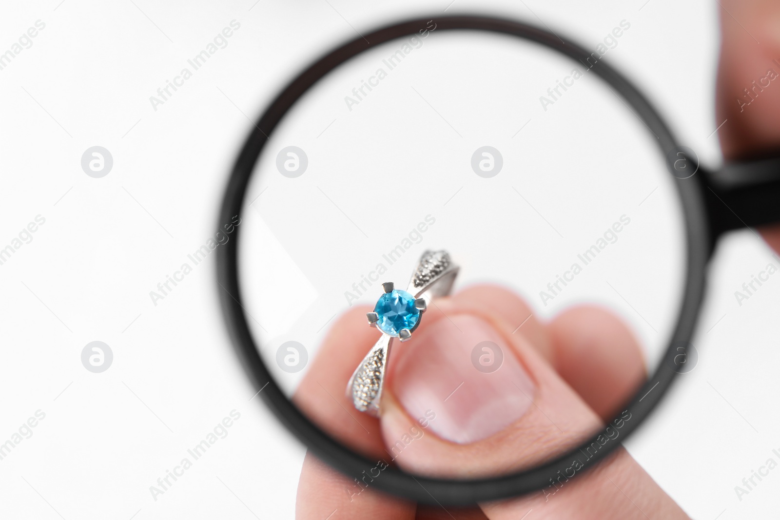 Photo of Jeweler examining topaz ring with magnifying glass on white background, closeup