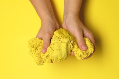 Photo of Woman playing with kinetic sand on yellow background, top view