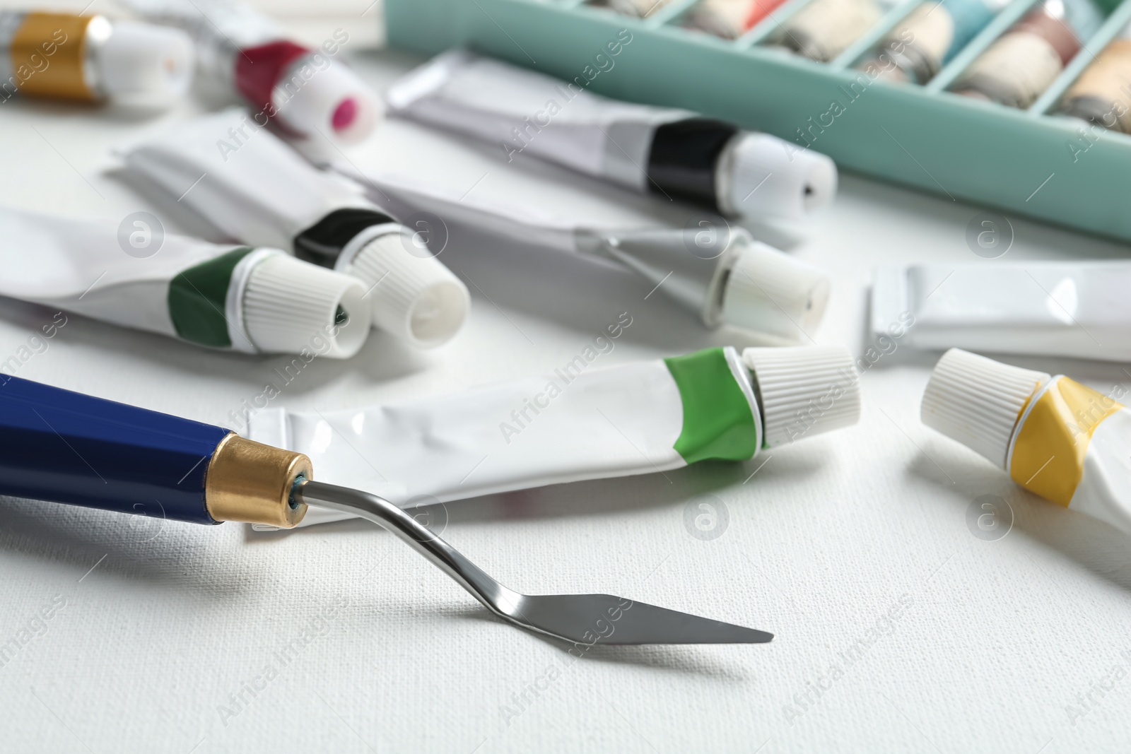 Photo of Tubes with paints and spatula on blank canvas, closeup